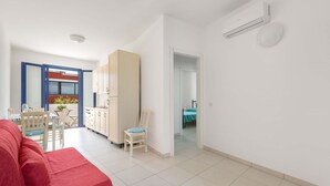 A modern apartment with a red sofa, a dining area with a table and chairs, a kitchen with cabinets, and a balcony with a bed. - 3403 Casa Petrachi - PP by Barbarhouse (Melendugno)