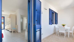 A room with a white tiled floor, a white dining table with chairs, and a blue door. - 3403 Casa Petrachi - PP by Barbarhouse (Melendugno)