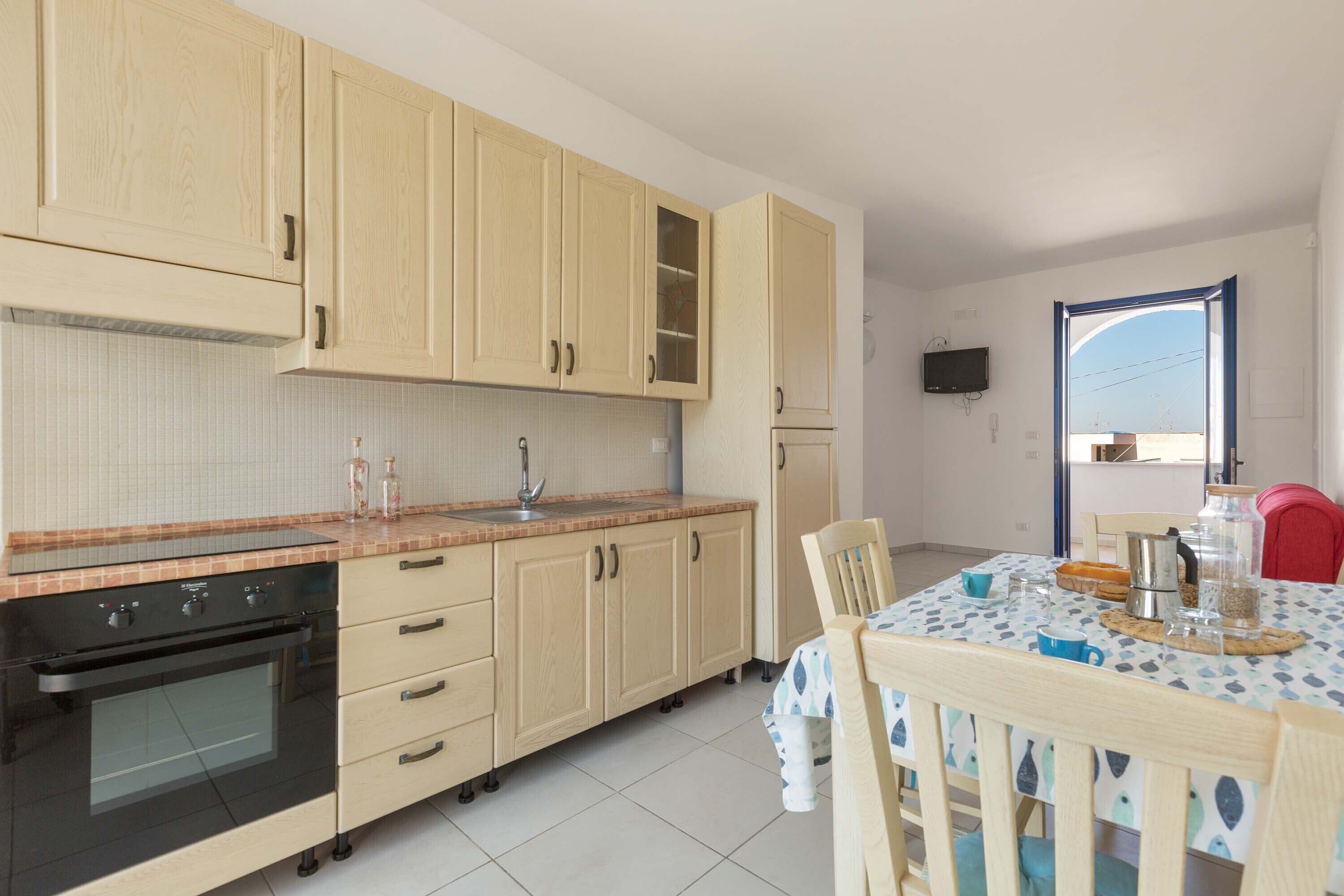 Een keuken met houten kastjes, een zwarte oven en een eethoek met een tafel gedekt voor twee personen.