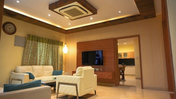 A modern living room with a sofa, armchair, and a TV mounted on the wall. - The Butterfly Luxury Serviced Apartments Ramachandra Vijayawada (Penumuluru)