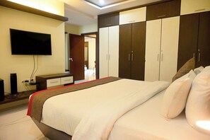 Hotellihuone, jossa on sänky, seinälle asennettu televisio ja useita ovia sisältävä vaatekaappi.