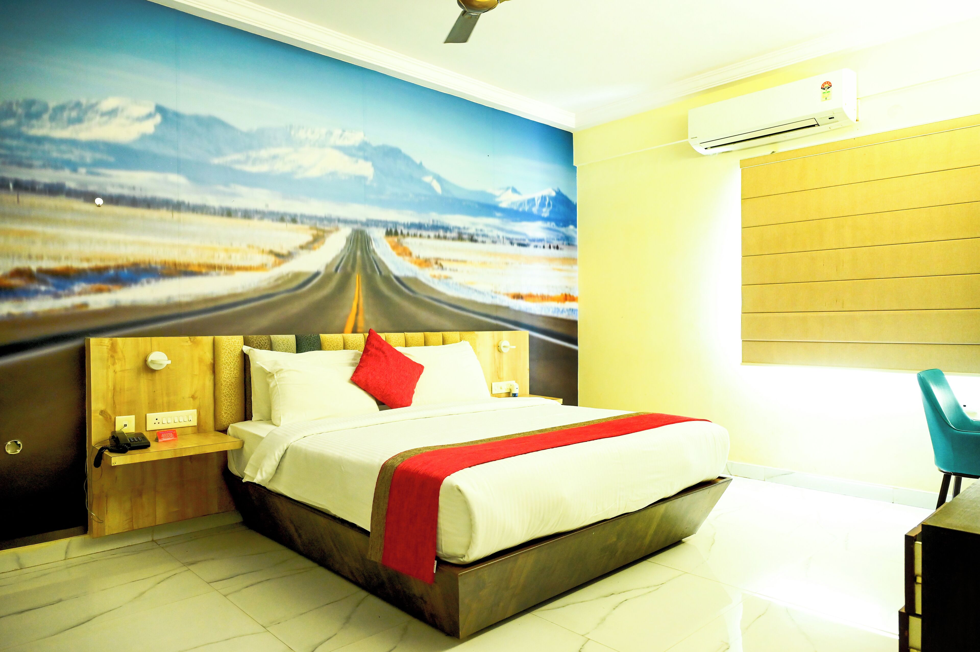 A hotel room with a large bed, a wooden headboard, a red throw blanket, a nightstand with a phone, and a wall-mounted air conditioner.