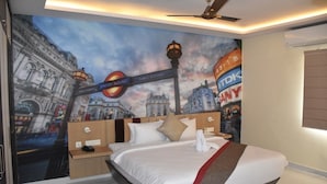 A hotel room with a bed, a nightstand, a wall mural of London landmarks, and a ceiling fan. - The Butterfly Luxury Serviced Apartments Ramachandra Vijayawada (Penumuluru)
