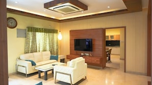 A modern living room with a sofa, coffee table, TV, and a dining area visible through an open doorway. - The Butterfly Luxury Serviced Apartments Ramachandra Vijayawada (Penumuluru)