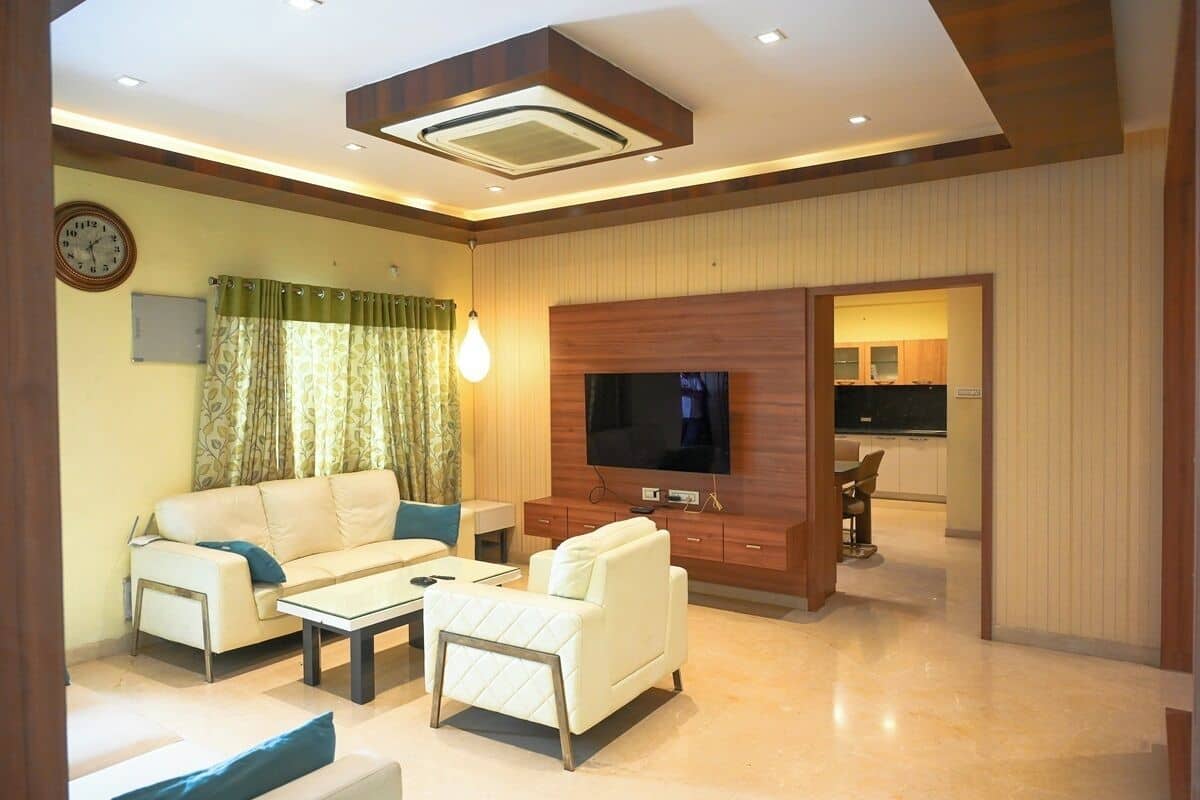 A modern living room with a sofa, coffee table, TV, and a dining area visible through an open doorway.