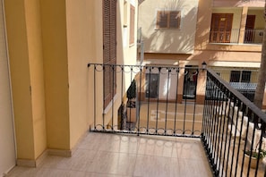 A balcony with a metal railing, a tiled floor, and a view of adjacent buildings.