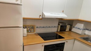 Kompakti keittiö, jossa on jääkaappi, mikroaaltouuni, liesi ja astianpesukone.