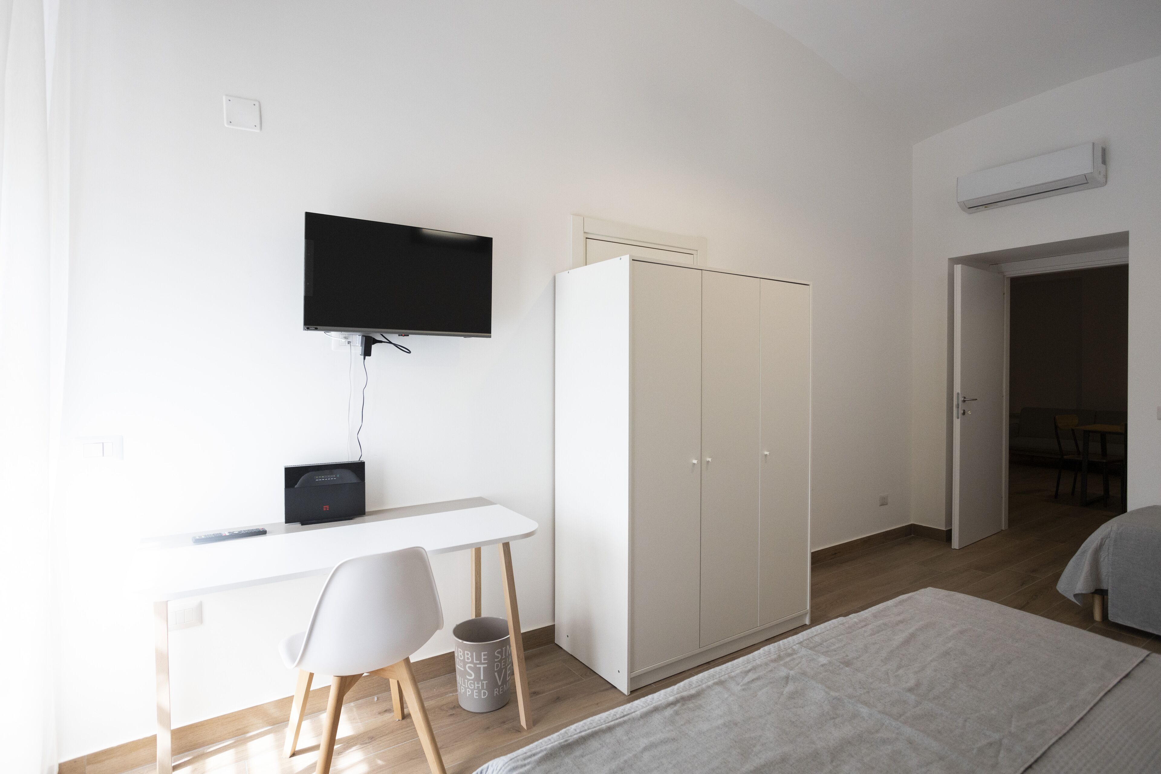 A bedroom with a bed, a desk with a chair, a wardrobe, and a television on the wall.