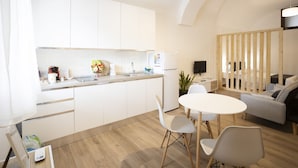 A modern kitchen with white cabinets, a dining area with a white table and chairs, and a living area with a sofa and TV. - Domus 47 Pompei (Pompei)