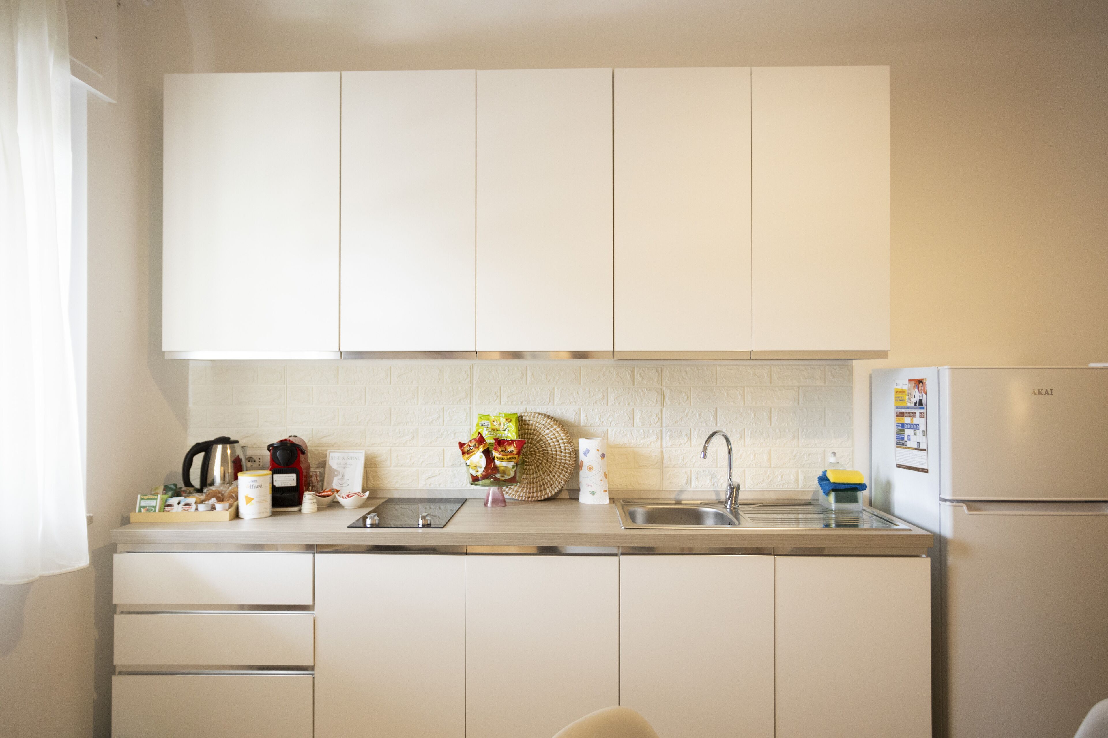 Eine Küche mit weißen Schränken, einer Edelstahl-Spüle und einem Kühlschrank.