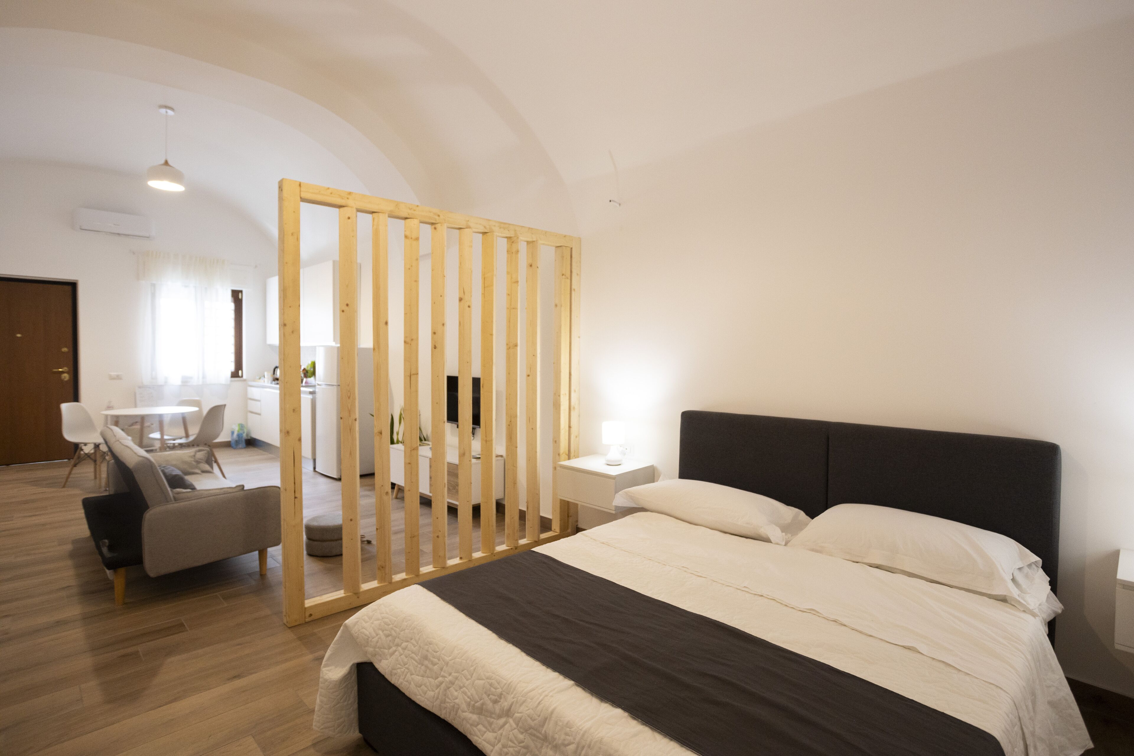 A modern bedroom with a large bed, a wooden partition, a desk, and a chair.
