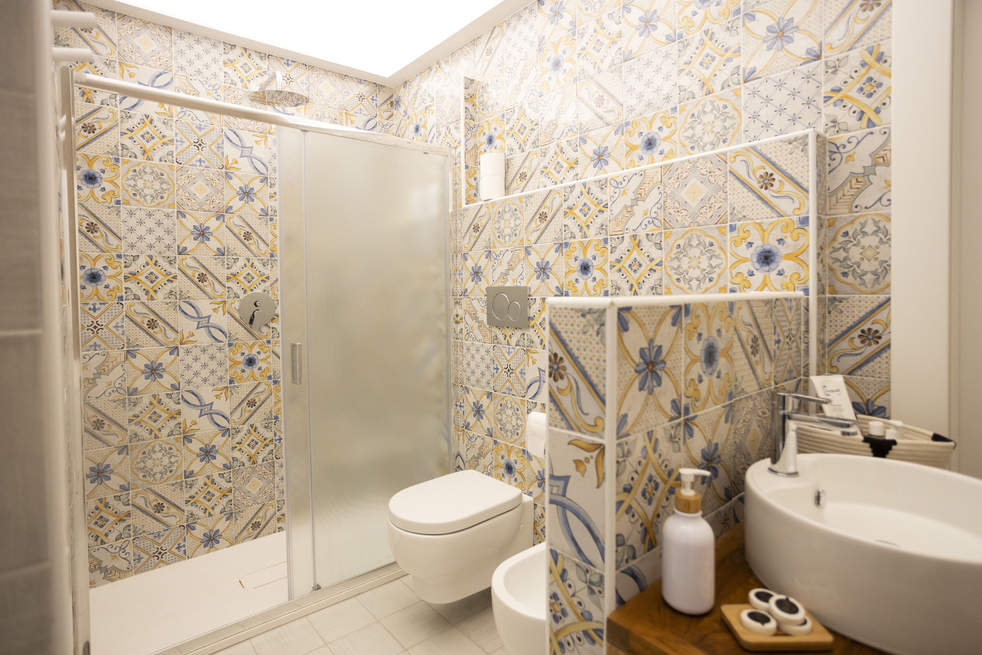 Un baño con azulejos estampados, un inodoro, un lavamanos y una zona de ducha.