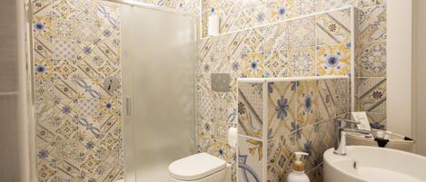 Un baño con azulejos estampados, un inodoro, un lavamanos y una zona de ducha.