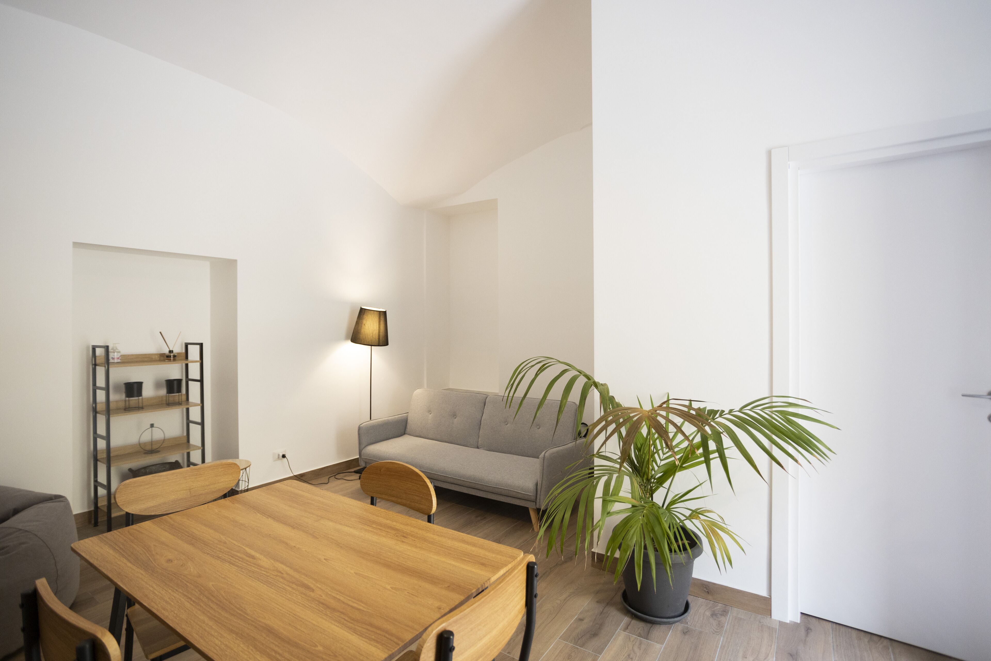 Una sala de estar moderna con una mesa de comedor de madera, un sofá gris, una lámpara de pie y una planta en maceta.