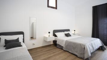 Una habitación de hotel moderna con dos camas individuales, una mesita de noche pequeña con lámpara, un espejo grande y una ventana con cortinas.