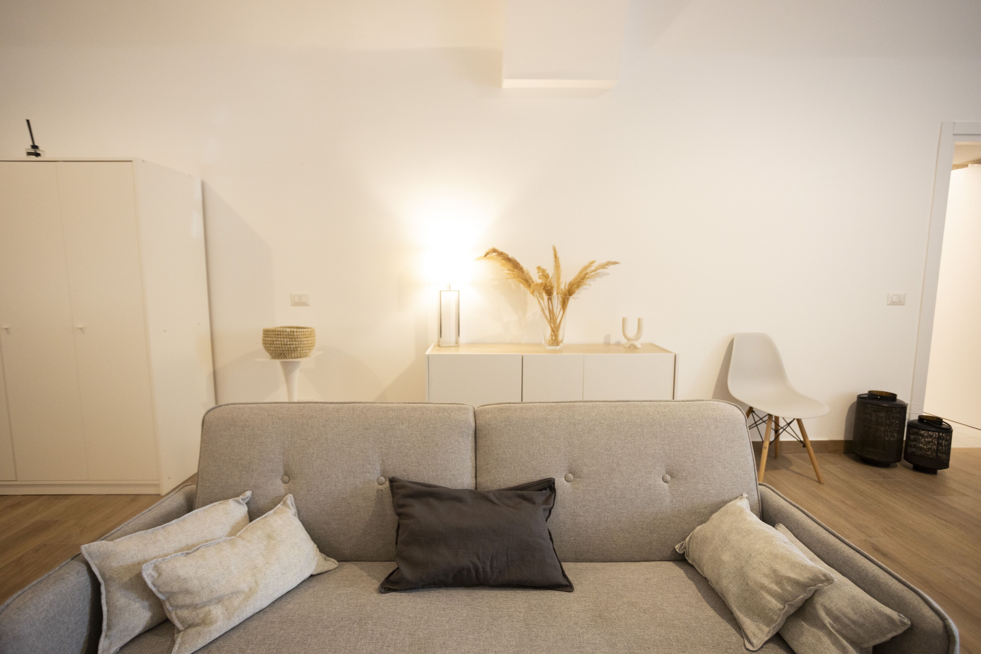 A modern living room with a grey sofa, a white cabinet, and a decorative vase with pampas grass.