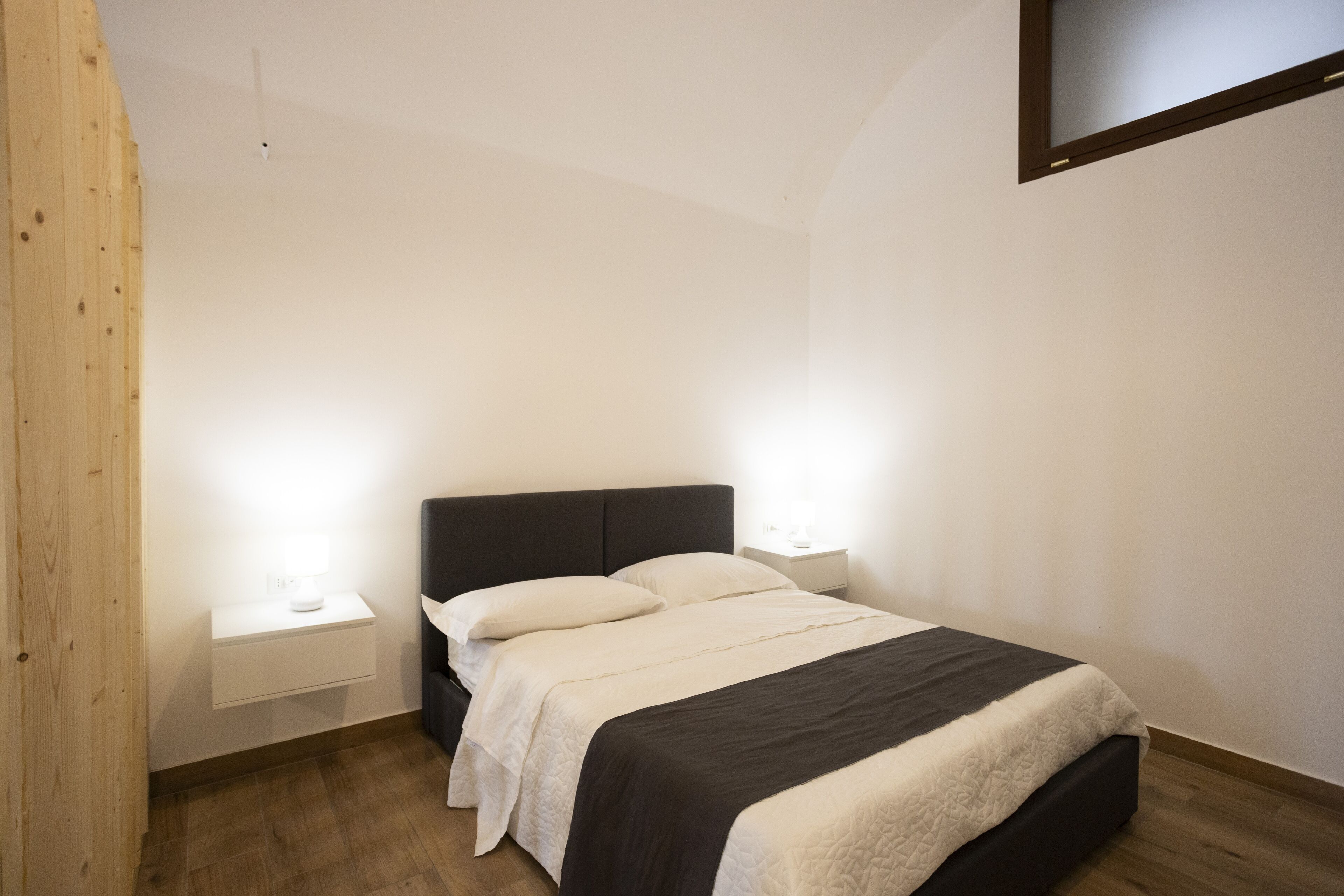 Un dormitorio con una cama, dos mesitas de noche y un televisor instalado en la pared.