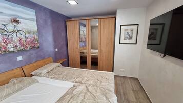 Een slaapkamer met een bed, een kledingkast, een schilderij en een televisie.
