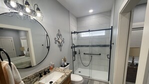 A modern bathroom with a granite countertop, a white sink, a toilet, a glass-enclosed shower, and a large mirror. - 2 bed, 2 bath cabin located in the country just west of College Station.   (Caldwell)