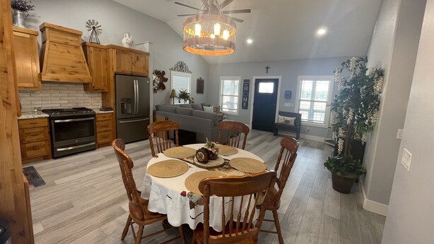 A modern kitchen with wooden cabinets, a stainless steel refrigerator, and a dining area with a round table and wooden chairs. - 2 bed, 2 bath cabin located in the country just west of College Station.   (Caldwell)