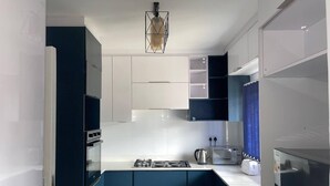 Een moderne keuken met blauwe kastjes, witte aanrechtbladen en een ingebouwde kookplaat.