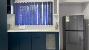 Een keuken met een koelkast, een raam met blauwe gordijnen en een aanrecht met een broodrooster.