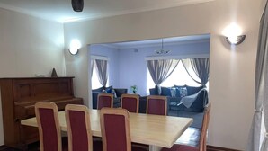 Een eetgedeelte met een houten tafel en zes stoelen, een bank op de achtergrond en een piano.