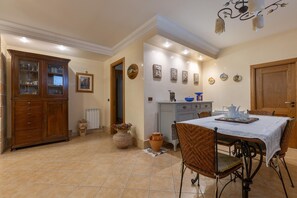 A dining area with a table set for four, surrounded by wicker chairs, a cabinet with glass doors, and a wall adorned with framed pictures. - 3578 Home In Salento Luna by Barbarhouse (Carpignano Salentino)