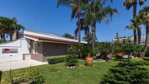 A house with a sign reading "Home in Salento," surrounded by a well-maintained garden with palm trees and a large decorative pot.