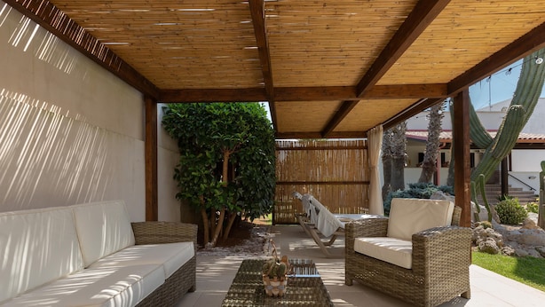 An outdoor patio with wicker furniture, a glass coffee table, and a large plant.