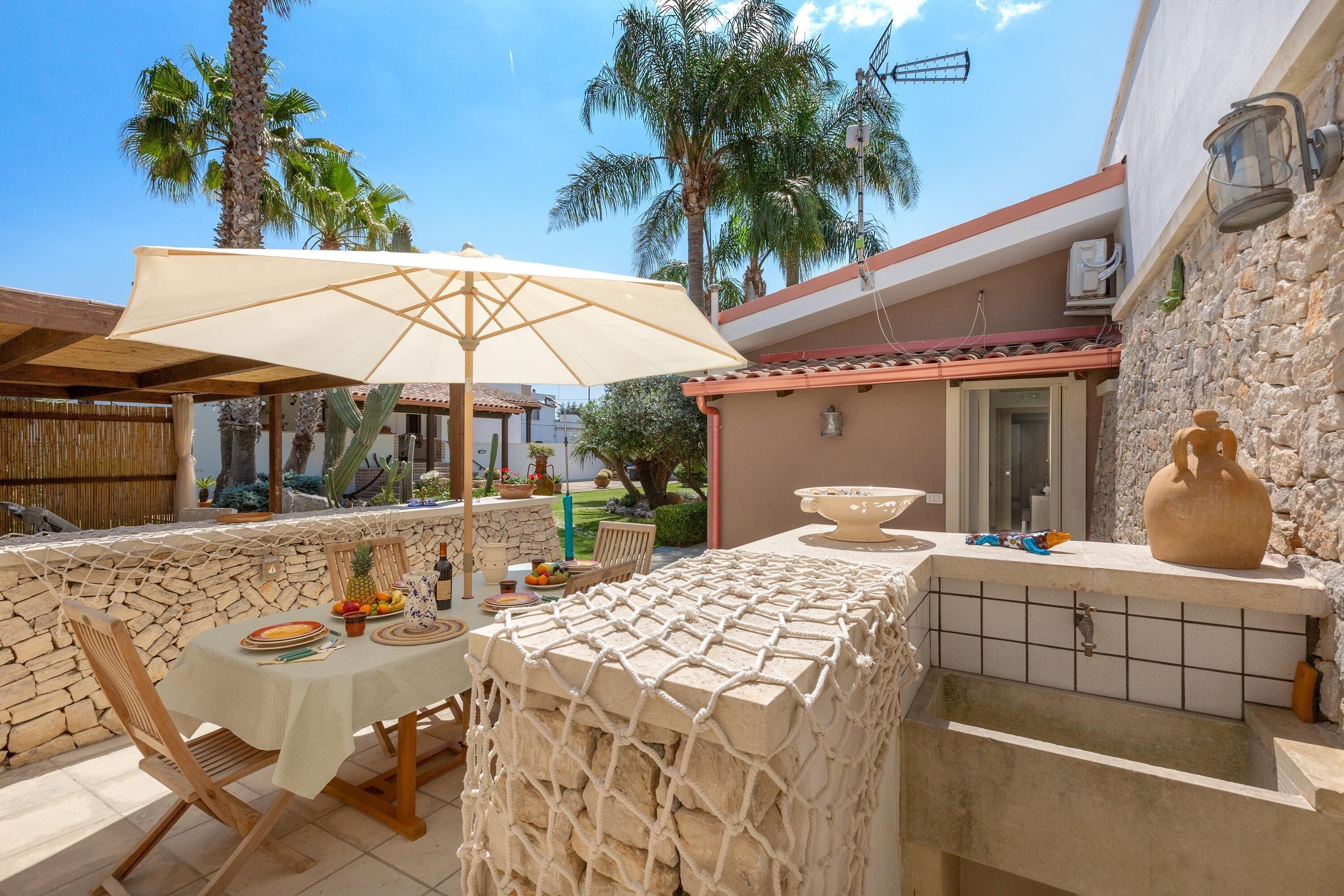 An outdoor dining area with a table, chairs, a large umbrella, and a stone wall.