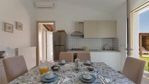 A dining area with a table set for four, a kitchen in the background, and a view of the outdoors.
