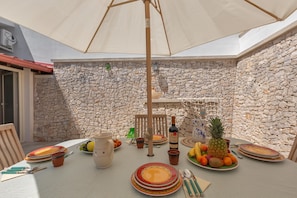 Un espace de restauration en plein air, avec un mur de pierres en arrière-plan, une table dressée avec des assiettes, des couverts et une variété de fruits et de légumes.