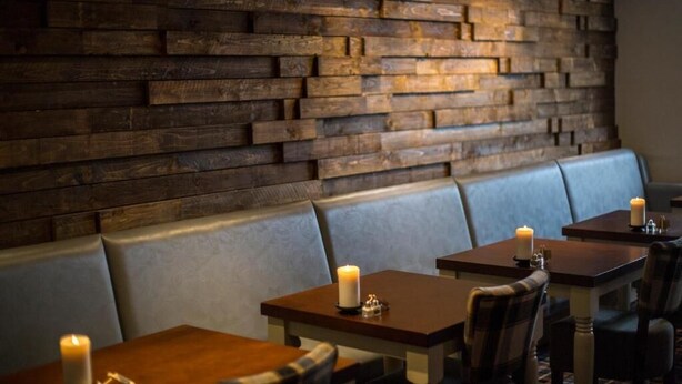 A restaurant interior with wooden walls, cushioned seating, and tables with candles.