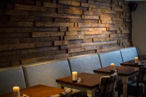 A restaurant interior with wooden walls, cushioned seating, and tables with candles.
