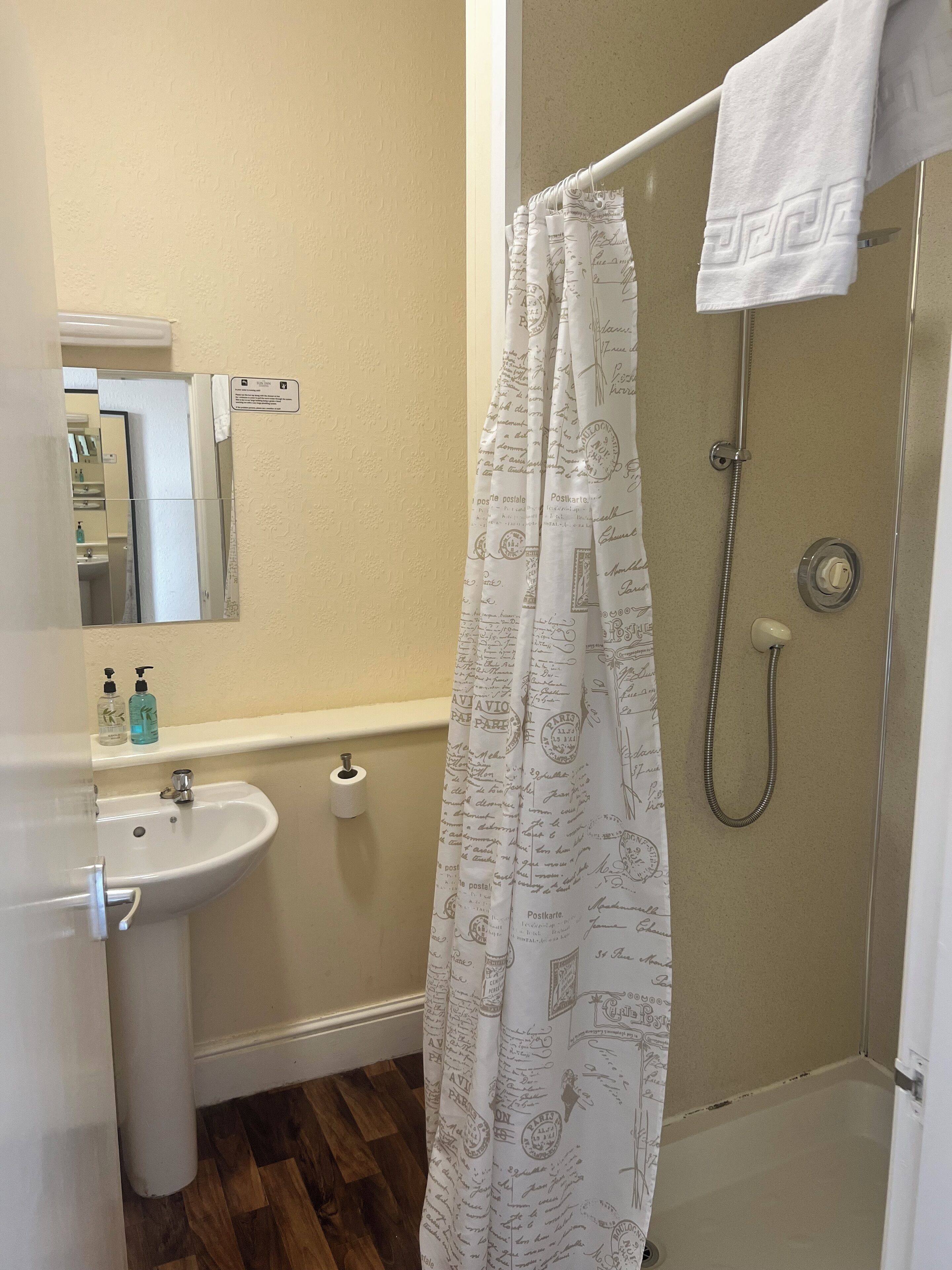 A bathroom with a sink, toilet paper, and a shower with a white shower curtain.