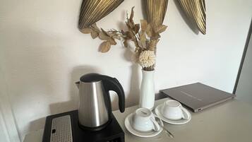 Una cafetera, un jarrón blanco con flores secas y una computadora portátil sobre una mesa.