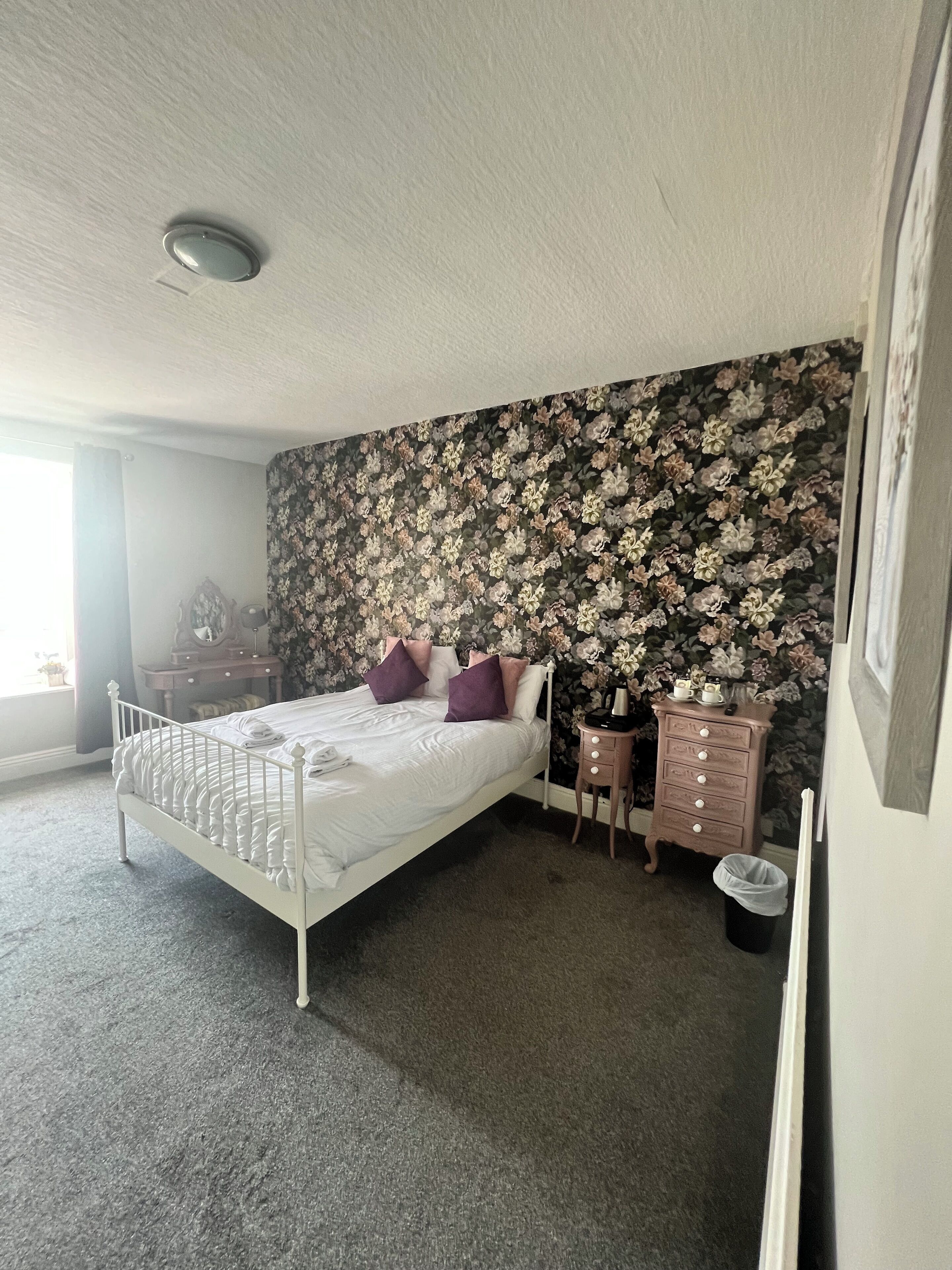 A bedroom with a bed, dresser, and a floral wallpaper.