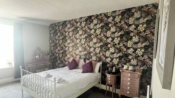 A bedroom with a bed, dresser, and a floral wallpaper.