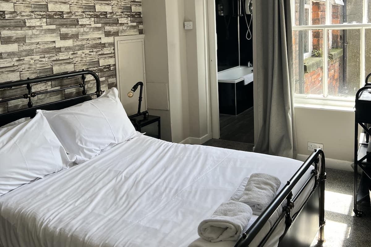 A neatly made bed with white linens and a folded towel, a bedside lamp, and a wall with a wooden pattern.