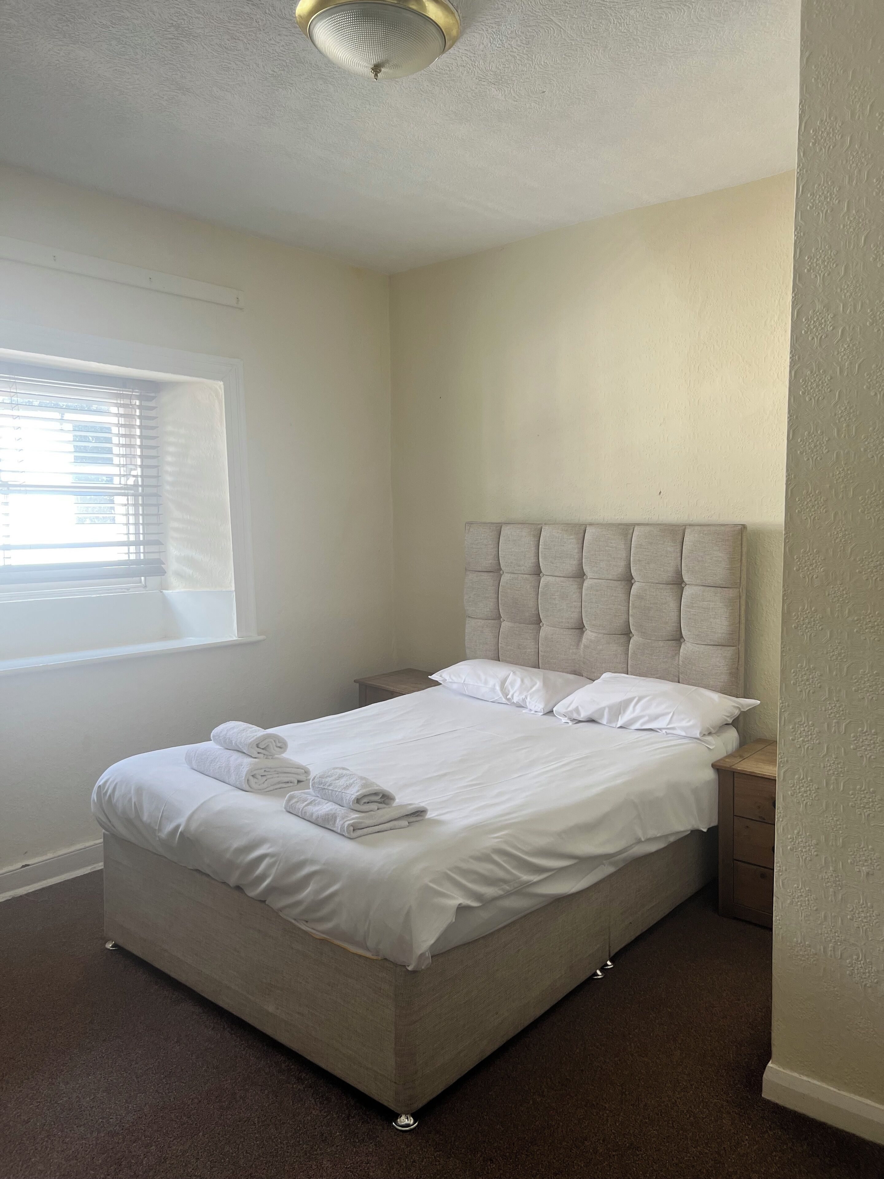A neatly made bed with white linens and towels, a tufted headboard, and a small bedside table.