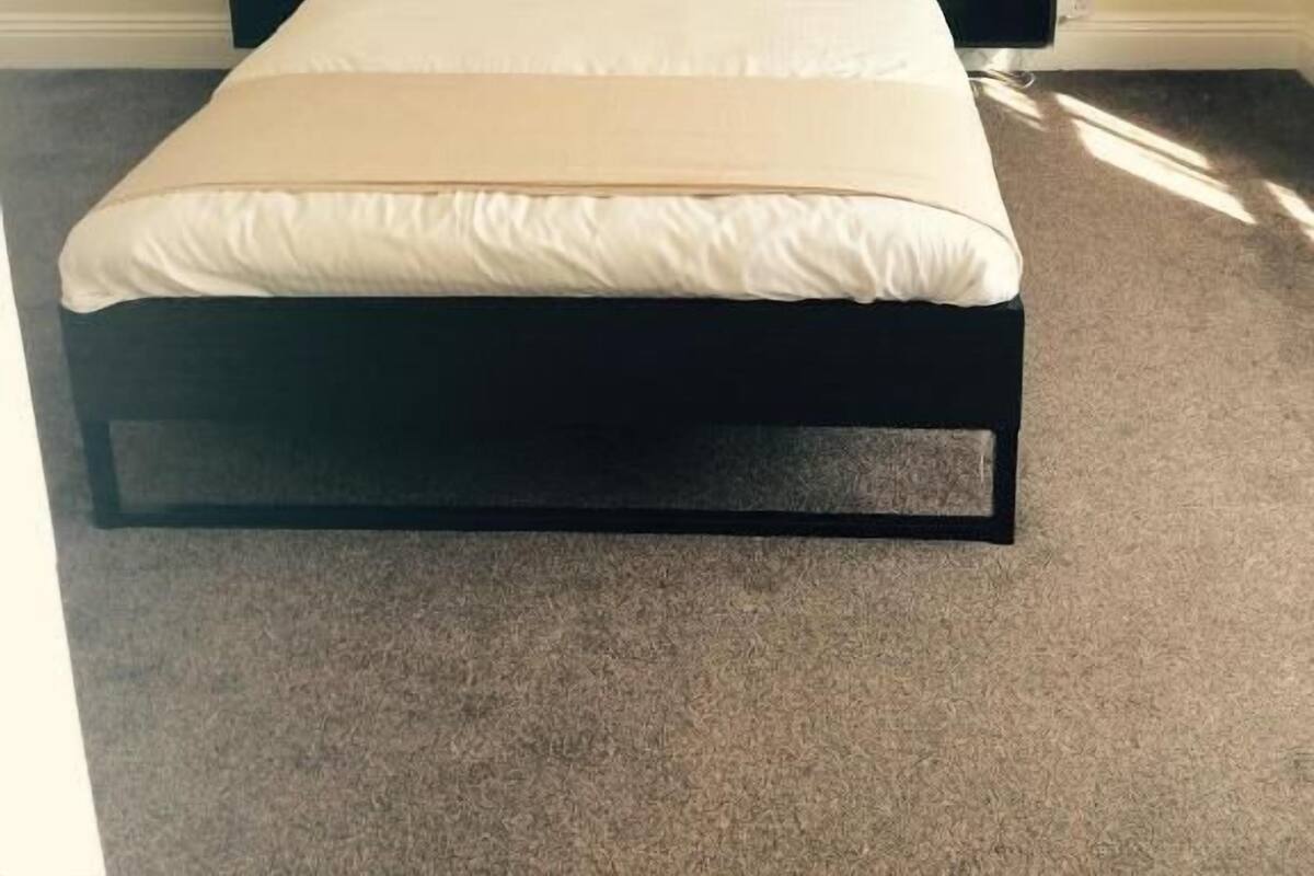 A bed with a black frame, white bedding, and two nightstands with a lamp on one.