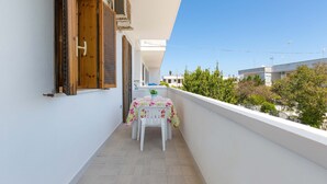 Ein Balkon mit Tisch und Stühlen, eine Holztür und Blick auf Grünflächen und Gebäude.