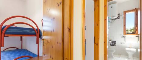 A room with a bunk bed, wooden wardrobe, and a bathroom with two toilets and a shower.