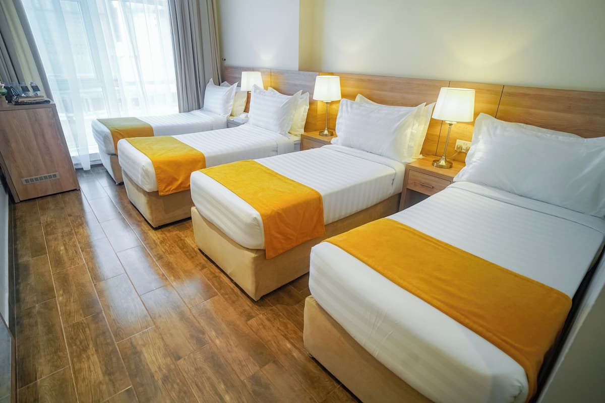 A hotel room with three beds, wooden flooring, and bedside lamps.