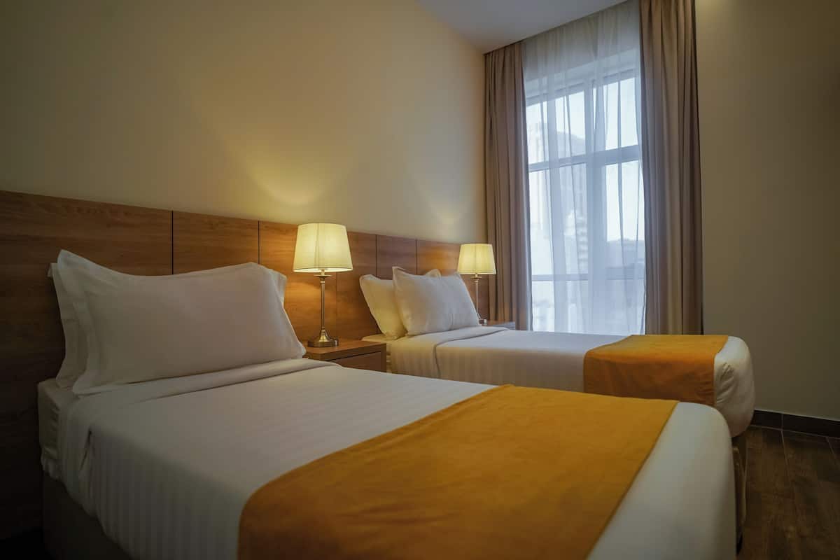 A hotel room with two beds, each with a lamp and a window with curtains.