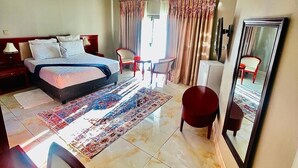 Habitación de hotel con cama, escritorio, silla, espejo y ventana con cortinas.