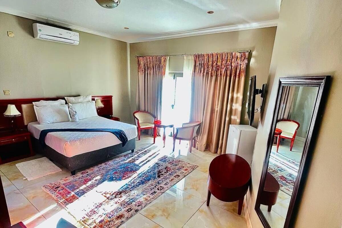 Une chambre d’hôtel avec un lit, un bureau, une chaise, un miroir et une fenêtre avec des rideaux.