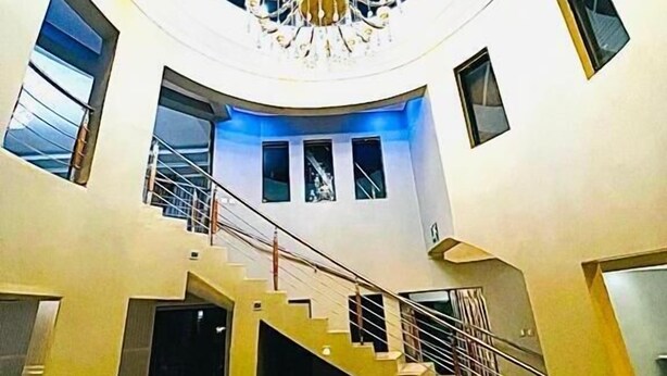 Un interior espacioso con una imponente escalera, un candelabro y un amplio ventanal.
