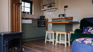 Una cocina acogedora con armarios de madera, una estufa y un ventanal. Hay taburetes y un sofá verde en la zona de estar.